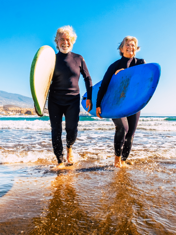 couple walking on beach carrying surfboards