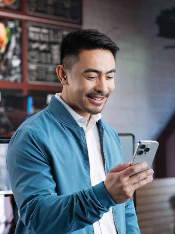 Man smiling while using a smartphone, wearing Phonak Virto R Infinio hearing aids, showcasing connectivity and modern hearing technology.